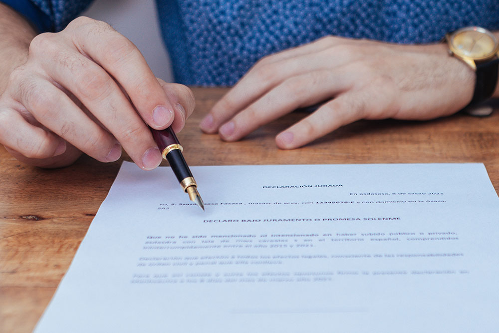 Close-up shot of hand in focus with pen, pointing to the title of the affidavit you are about to sign.
