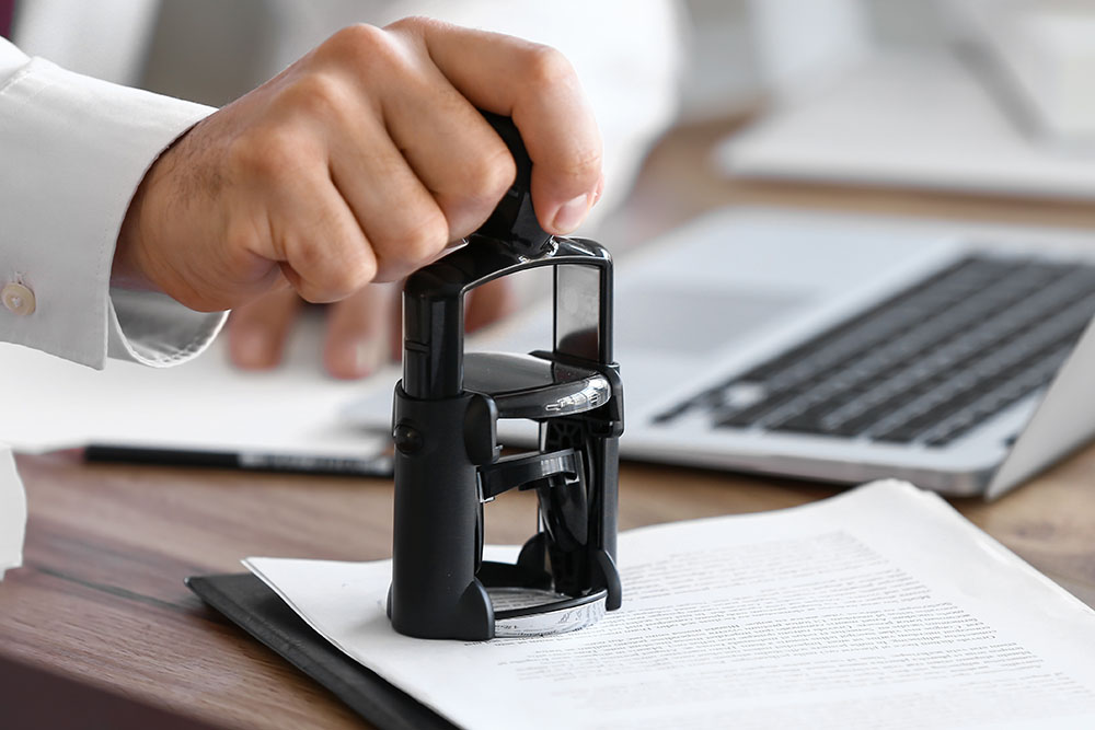 Male notary public attaching seal to documents in office